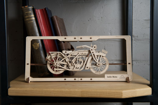 Ugears Motorrad Puzzle Modell aus Holz in natürlicher Farbe auf einem Regal mit Büchern im Hintergrund